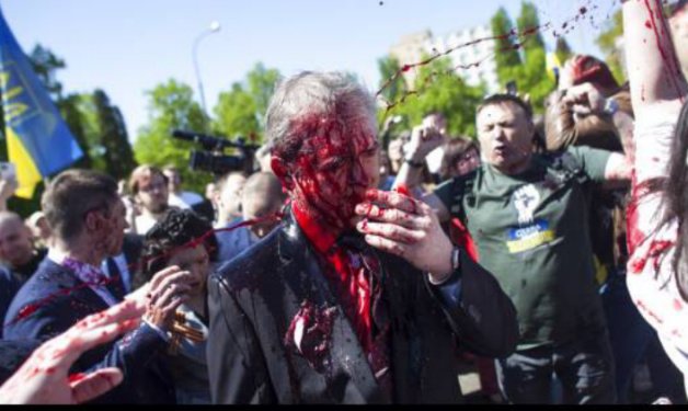 Duta Besar Rusia untuk Polandia Sergey Andreev disiram cat merah oleh demonstran saat hendak menziarahi makam Tentara Merah dalam peringatan Hari Kemenangan di Warsawa, Polandia, Senin (9/5/2022). (Sumber: Maciek Luczniewski/Associated Press)