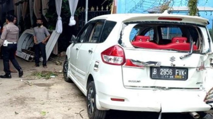 Kaca belakang mobil putih pecah setelah terbentur tiang listrik dan ban belakang terperosok ke dalam parit.