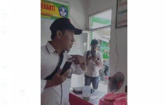 dua pria berpakaian putih memegang handphon memvideokan aktivitas di ruang guru SD di Desa Sri Menanti, Sribhawono, Lampung Timur. Kedua pria itu kompak menggunakan tas selempang dan memakai topi hitam. - foto Screenshot
